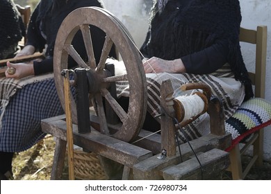 In the foreground an old spinning wheel in the background, out of focus, a woman combing wool - Powered by Shutterstock