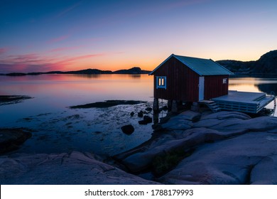 In the foreground a red boathouse on the cliffs with wooden decks for boats. In the background a colorful sky and calm sea