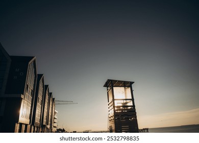 In the foreground, there is a lifeguard tower standing tall, while in the background, a charming row of beach huts can be seen, adding character to the scene - Powered by Shutterstock