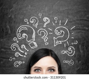 A forehead of the brunette girl who is pondering about unsolved problems. Question marks are drawn around the head. black chalkboard background.