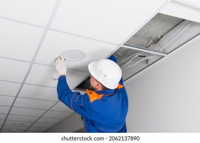 foreman in blue uniform and white hard hat, installed a lighting lamp in the false ceiling - Powered by Shutterstock