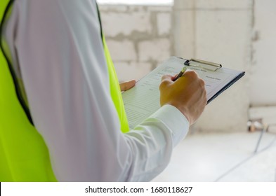 foreman builder, engineer or inspector in green safety vest reflective checking and inspecting with clipboard at construction site building interior, inspection, contractor and engineering concept