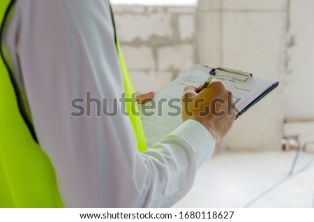 foreman builder, engineer or inspector in green safety vest reflective checking and inspecting with clipboard at construction site building interior, inspection, contractor and engineering concept