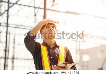 Foreman builder engineer worker looking at large building construction site sunny day hard work.