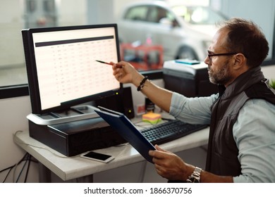 Foreman Of Car Service Workshop Using Computer And Going Through Reports In The Office.