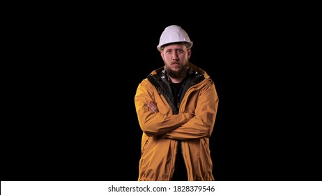 Foreman engineer puts on white helmet and looks at the camera. The real boss, man in yellow raincoat on black background, looks at his workers very seriously.