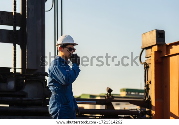 Foreman in hardhat and safety\
vest talks on two-way radio control loading containers box from\
cargo