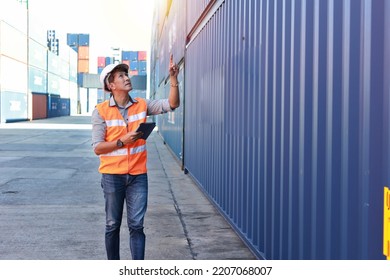Foreman walking while pointing something and using tablet control loading containers box. Engineer with safety hat work at container cargo site and checking industrial container cargo freight ship.