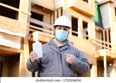 Foreman Wearing Mask And Hardhat Showing Disinfectant At Construction Site. Concept Of Coronavirus Protection And Social Distance At Workplace.