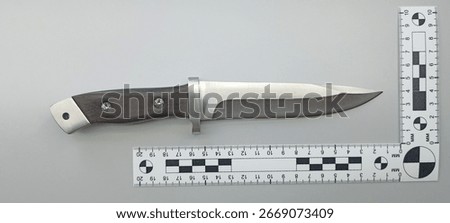 Forensic analysis of bladed weapons, knife with scale ruler on gray background. Evidence examination in police forensic laboratory.