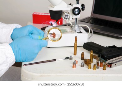 Forensic Analysis - A Forensics Lab Technician Examines A Bullet And Hand Gun For Finger Prints, Blood Splatter, And Any Other Residue Or Evidence To Be Used In A Court Case