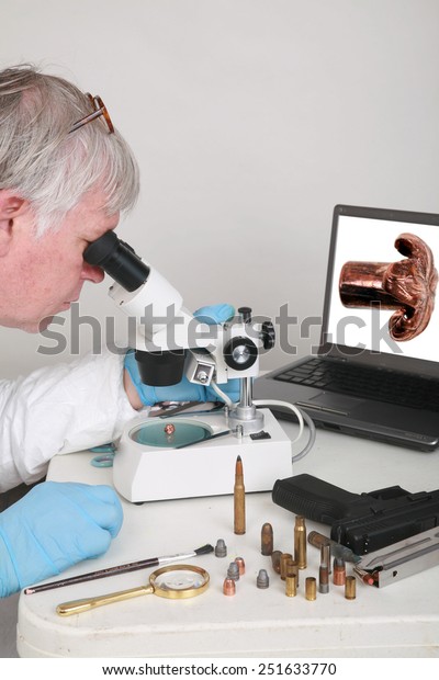 forensic analysis - a\
forensics lab technician examines a bullet and hand gun for finger\
prints, blood splatter, and any other residue or evidence to be\
used in a court case