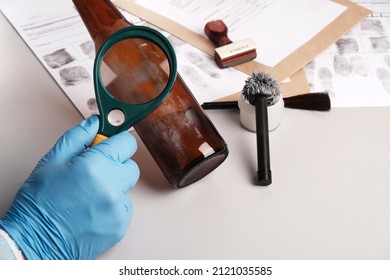 forensic expert using a magnifying glass examines fingerprints on evidence -  glass bottle, forensic fingerprint analysis in  police forensic laboratory - Powered by Shutterstock