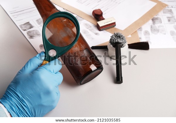 forensic expert using a magnifying glass\
examines fingerprints on evidence -  glass bottle, forensic\
fingerprint analysis in  police forensic\
laboratory