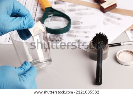 Forensic fingerprint analysis, criminalist collects latent fingerprints using fingerprint powder on evidence -  glass cup,copying fingerprints on lifter
