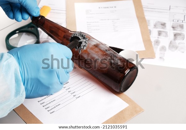 Forensic fingerprint analysis, criminalist\
collects latent fingerprints using fingerprint powder on a glass\
bottle close-up