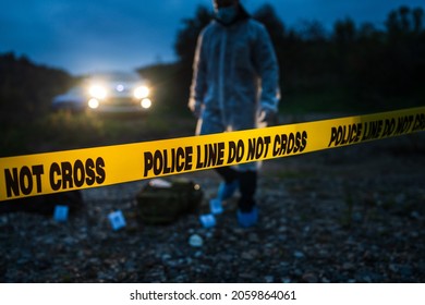 Forensic Police Investigator Collecting Evidence At The Crime Scene By The River In Nature At Night Selective Focus On Police Line Tape