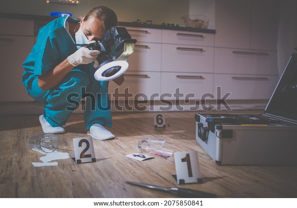 Forensic specialist in protective suit taking\
photos on a crime\
scene