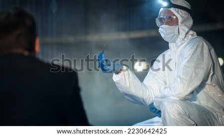 Forensics Expert Explaining his Conclusions After Finding Incriminating Evidence on the Crime Scene. Specialist in Coverall Carefully Handling a Bullet Shell as He Shows it to Detective.