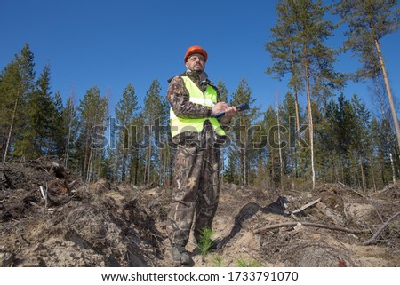 Forest engineer stands on the site of a cut down forest. Forester in a work vest and hard hat. Forest worker records information. Real people work in forestry.