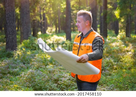 Forest engineer or surveyor holding maps and inspecting forest land