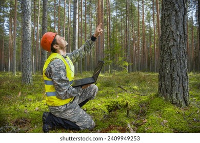 Forest engineer works in the forest with a computer. Trees appear on the computer screen.