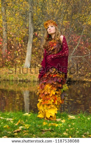 forest fairy in a dress of autumn leaves walking along the shore of a forest pond