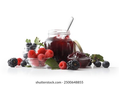 Forest fruit jam with full jars and containers with raspberries, blackberries and blueberries on white isolated background reflected in the base. Front view.