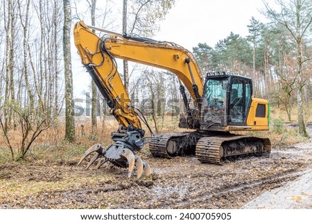 Forest with a grab excavator on muddy ground, bare trees on foggy background, workplace in construction and maintenance of rural road in forest area
