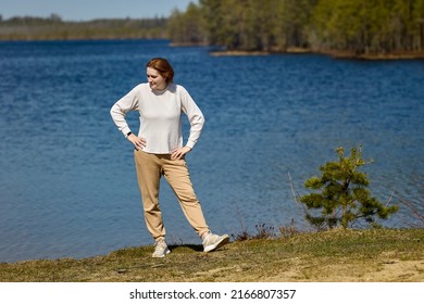 Forest Lake In Northern Europe, Young Woman In White Sweater Stands On Shore In Spring.