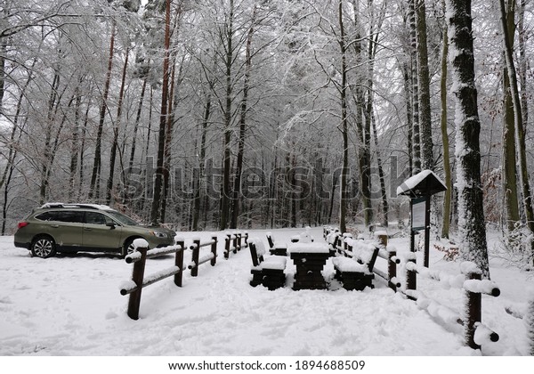 Forest parking lot with rest area with wooden\
benches covered with snow in forest. There is standing car. Otomin,\
Kashubia, Poland