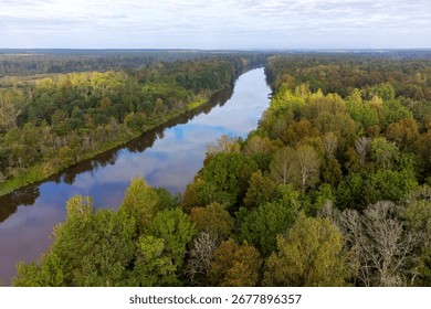 Forest river in autumn. Clouds are reflected in the forest river top view. Mesmerizing view of the forest river in early autumn. River forest landscape.