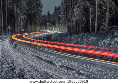 Forest road in winter with car light trails