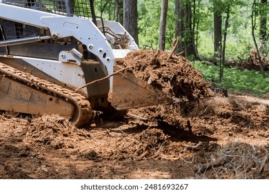 At forest, tractor is using bucket to level ground during earthworks