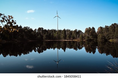 Forest and a windmill in the centre reflect in the dark water of Lake Blindensee in the Black Forest, Germany.