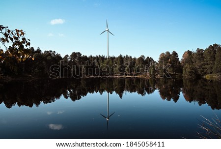 Forest and a windmill in the centre reflect in the dark water of Lake Blindensee in the Black Forest, Germany.