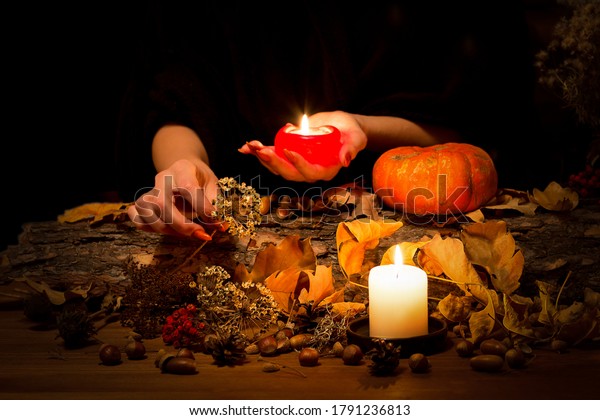 Forest witch at work on the altar. Female hands\
with sharp red nails among candles, herbs, pumpkin, nuts, dry\
leaves, ashberry, selected focus, low key. Halloween, Samhain\
night, autumn, magic