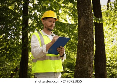 Forester in hard hat with clipboard examining plants in forest - Powered by Shutterstock