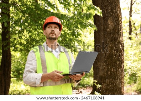 Forester in hard hat with laptop working in forest