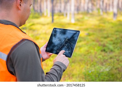 Forester using tablet computer in forest and looking at topological map or land plan on the screen