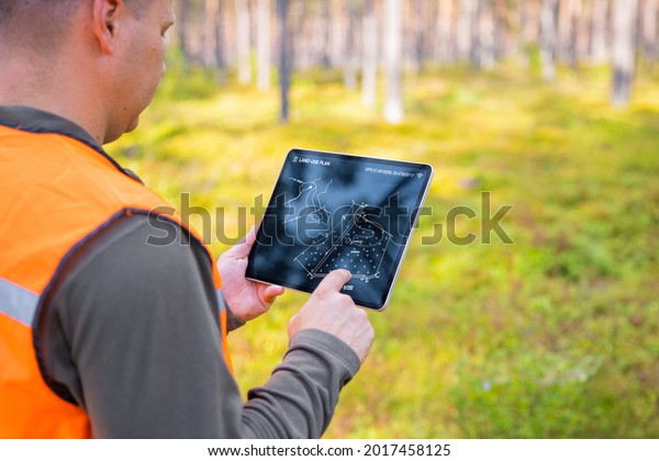 Forester using tablet computer in\
forest and looking at topological map or land plan on the\
screen