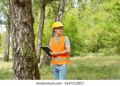 Forester worker learning plants. Engineer ecologist man in the forest marks of the ecological situation. Eco technic with clipboard checking trees.