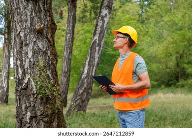Forester worker learning plants. Engineer ecologist man in the forest marks of the ecological situation. Eco technic with clipboard checking trees.
