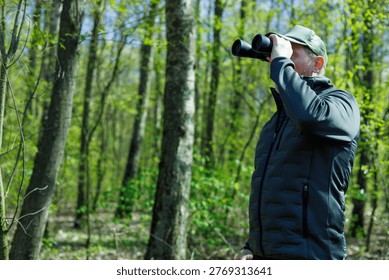 Forestry engineer or ecologist inspector observing wildlife through binoculars in the forest. Nature conservation and monitoring. Environmental protection and forest management. Discovery, environmental appreciation, observation, hunting, or forest management.