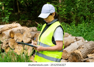 Forestry inspector records logging data. Mature female eco engineer with tablet checks felled trees. Female ecologist in overalls audits forestry.