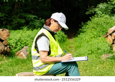 Forestry inspector records logging data. Mature female eco engineer with tablet checks felled trees. Female ecologist in overalls audits forestry.