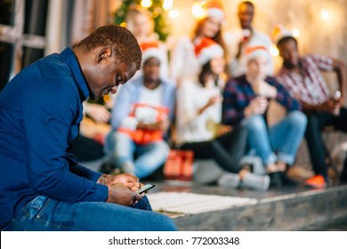 Forever Alone. African Black Man Sitting At Party And Using Phone