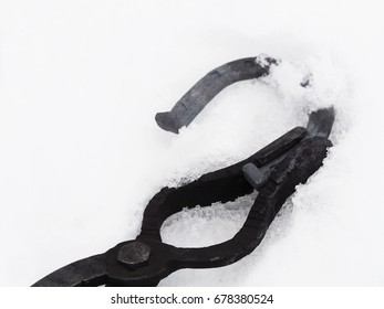 Forge, handmade: tongs for hot forging with horseshoe. Cooling the red-hot horseshoe in the melts snow - Powered by Shutterstock