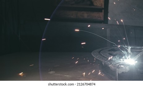 Forge Workshop. Smithy. Worker In A Welding Hood Helmet Welds A Part By Electric Welding. Sparks Are Reflected In The Protective Screen. Blacksmith Makes Iron Product For Manufacture. Slow Motion.