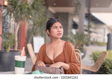 A Forgetful Asian Lady Sitting Outside The Coffee Shop Pauses To Think Of Where She Placed Her Pocket Mirror After Looking For It Inside Her Bag.